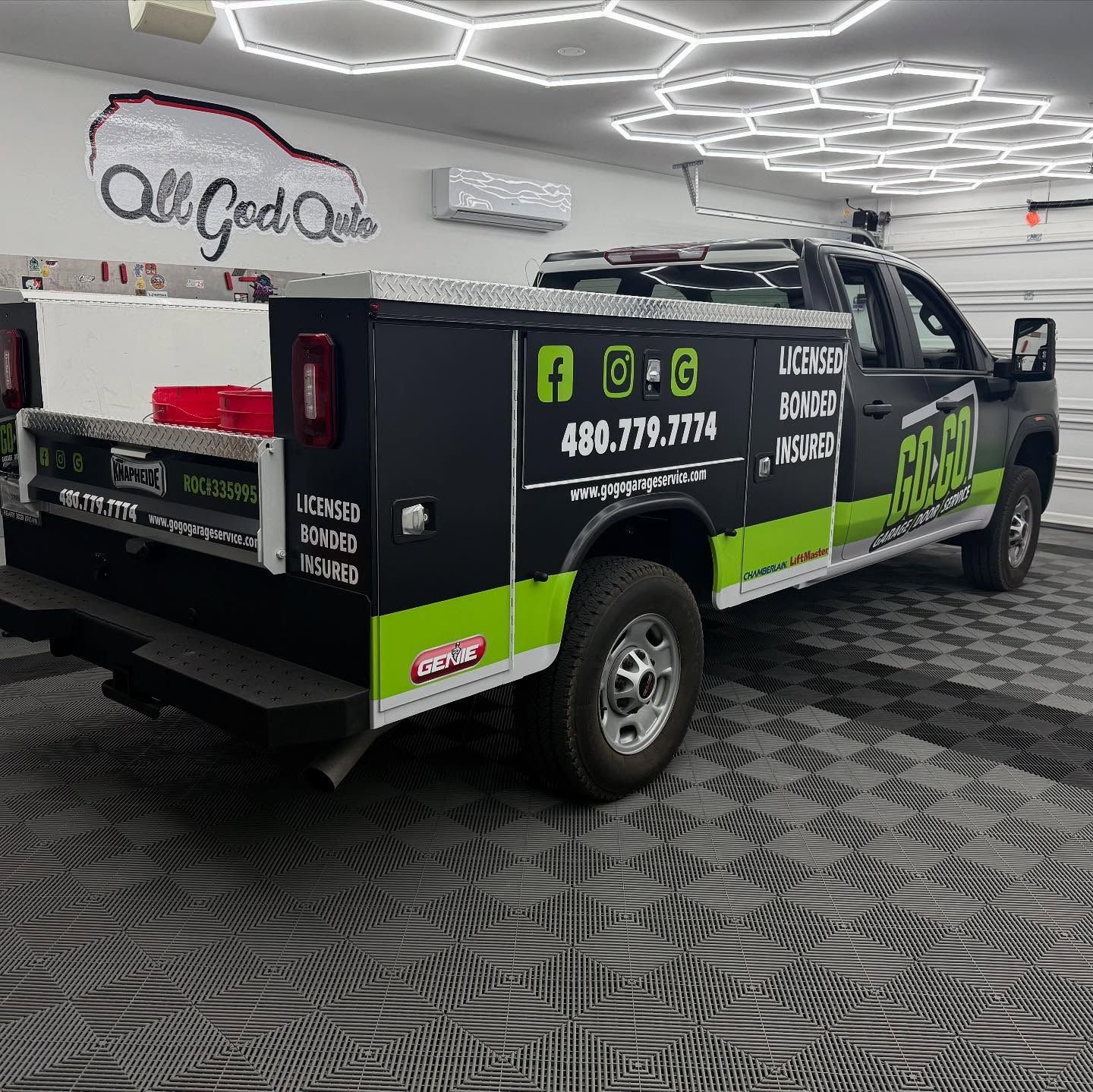 Black service truck in a garage; green and white logos, text.