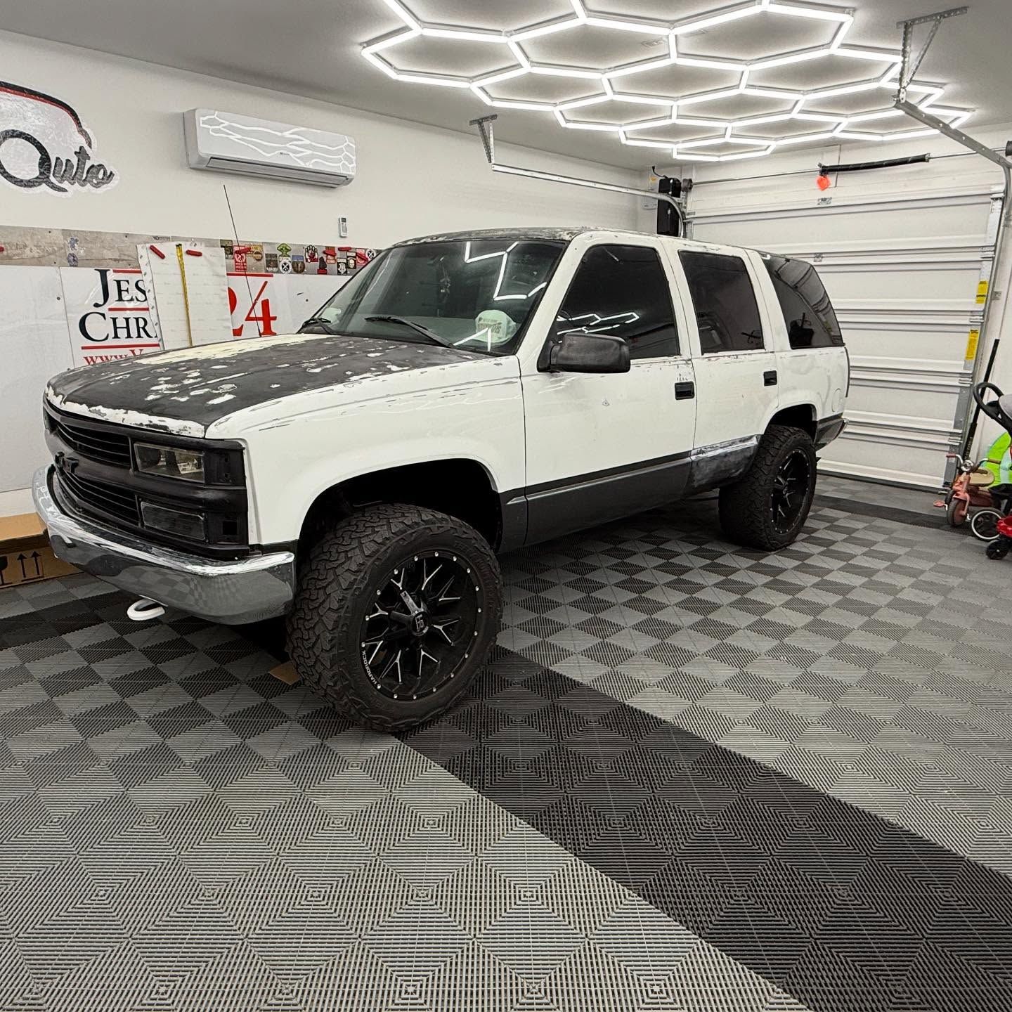 White and black SUV parked in a garage with hexagon-shaped ceiling lights.