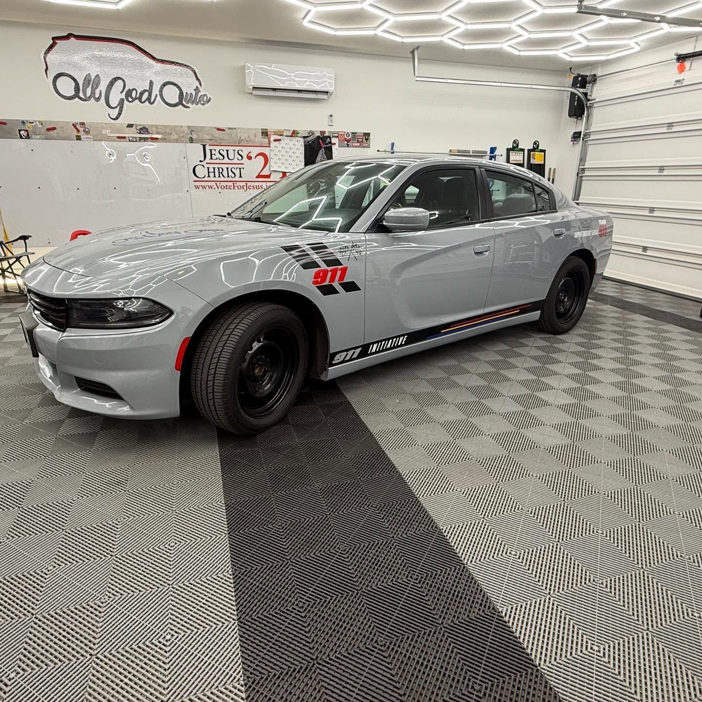 Grey Dodge Charger with black rims in a garage with checkered flooring.