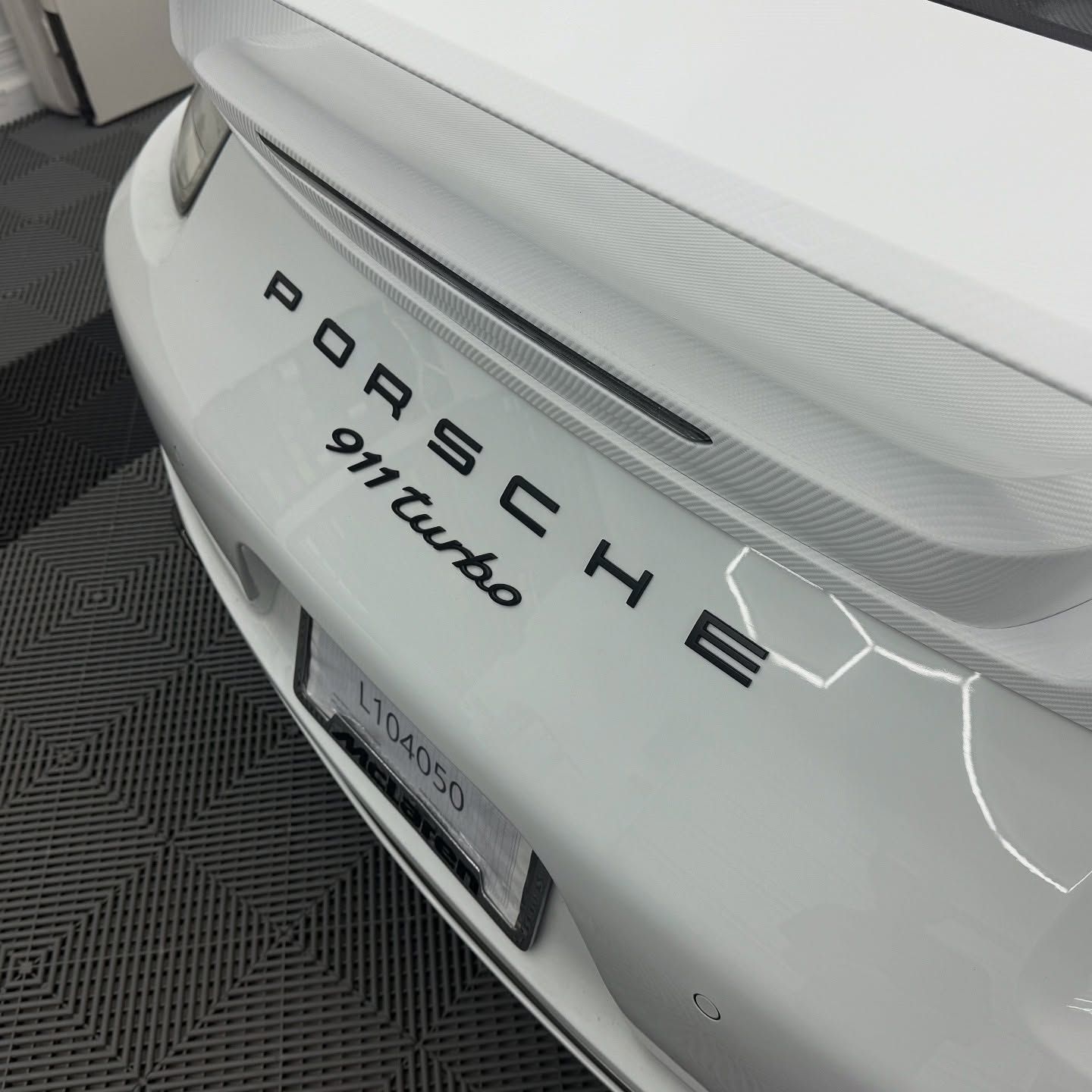 White Porsche 911 Turbo's rear with black lettering on a patterned floor.