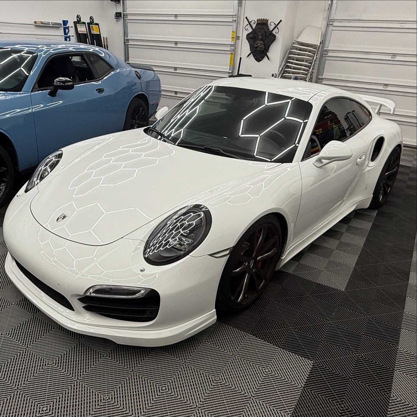 White Porsche 911 Turbo parked in a garage next to a blue Dodge Challenger.