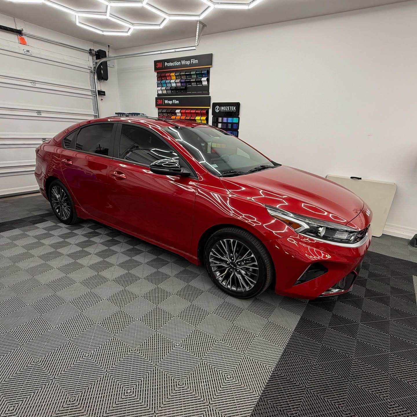 Red Kia Forte sedan in a garage with tinted windows, black wheels, and black trim.