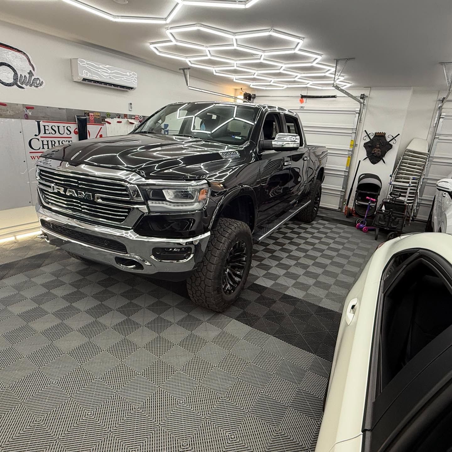 Black Ram pickup truck inside a garage with a white car on the right.