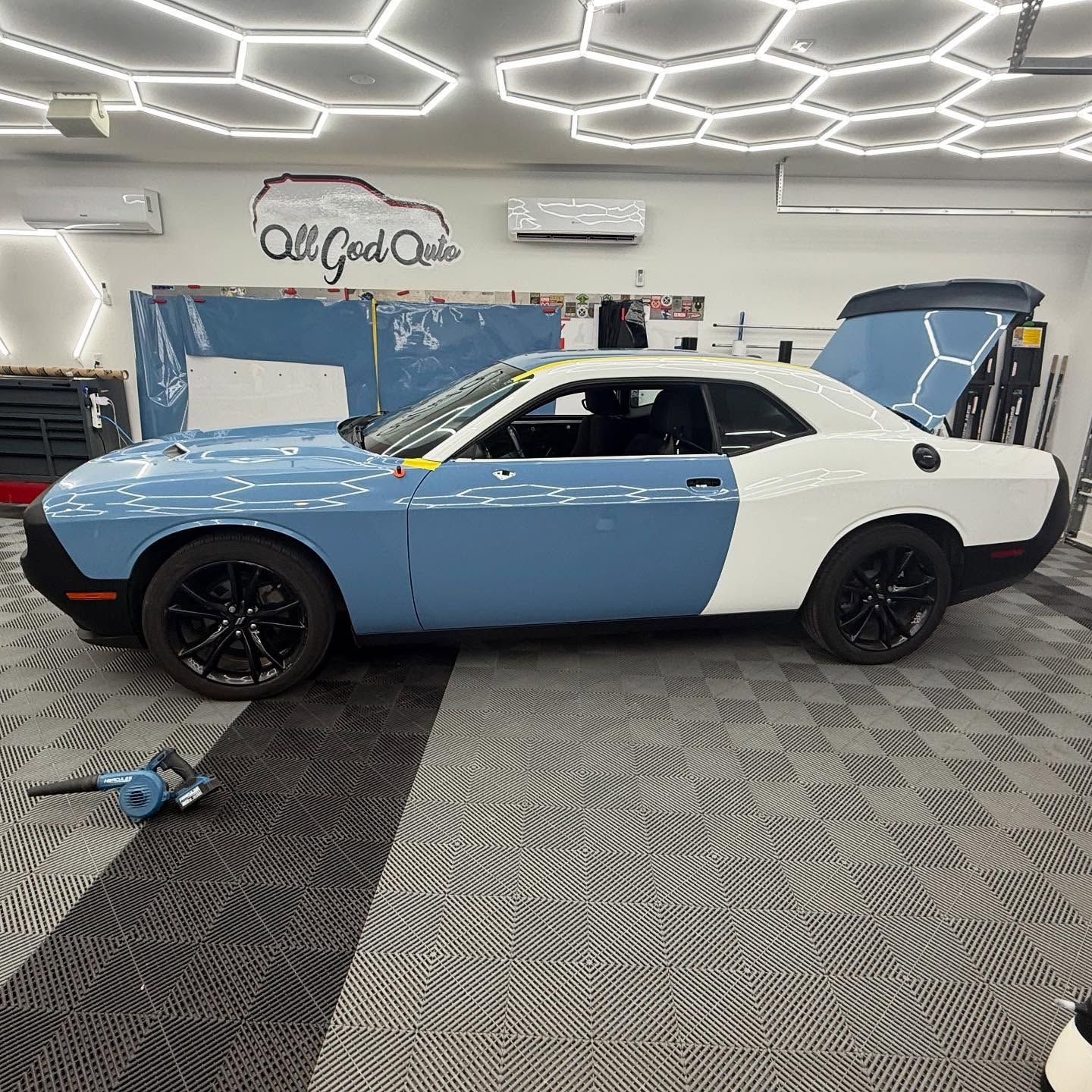 Blue and white Dodge Challenger being worked on in a garage.