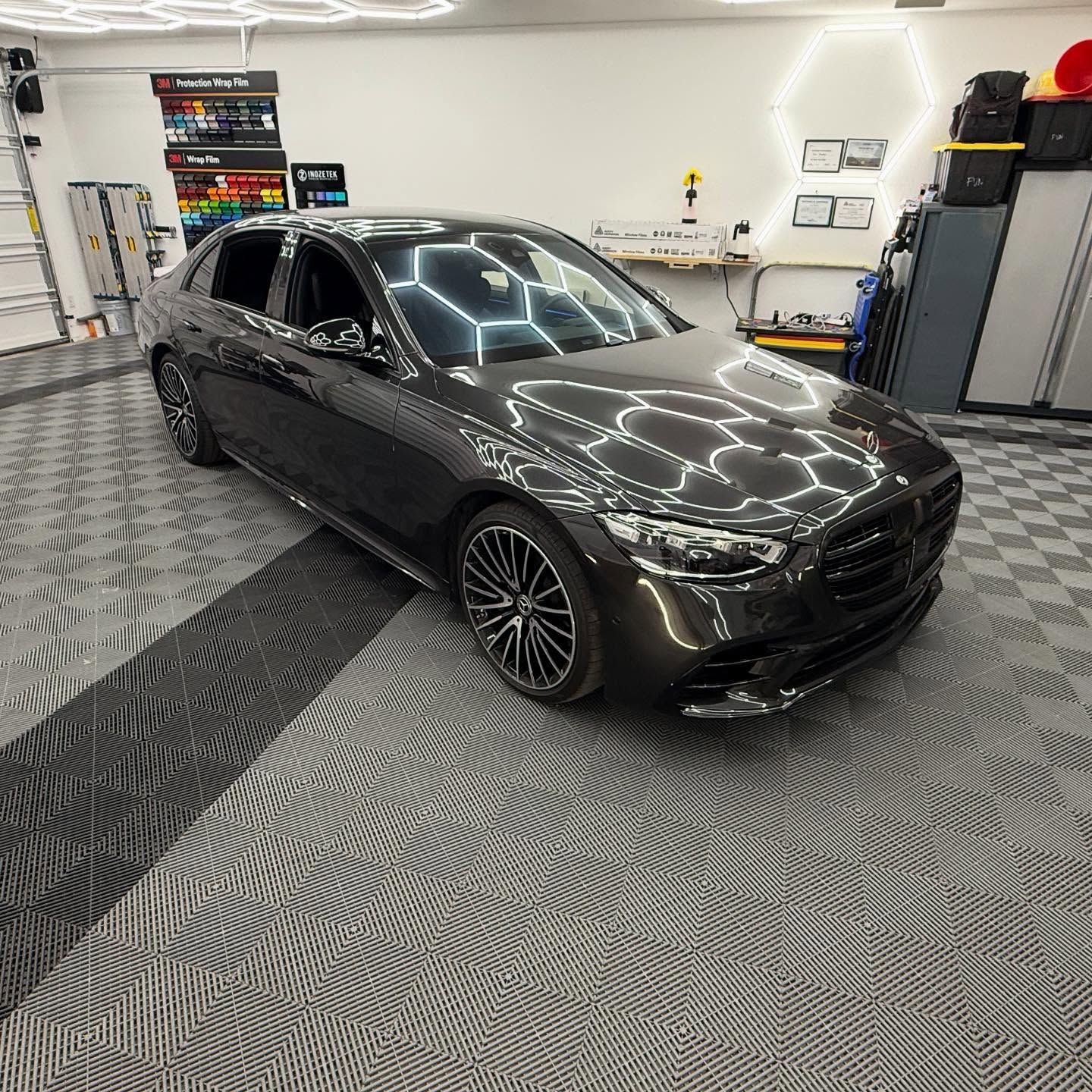 Dark gray Mercedes sedan in a well-lit garage with patterned flooring.
