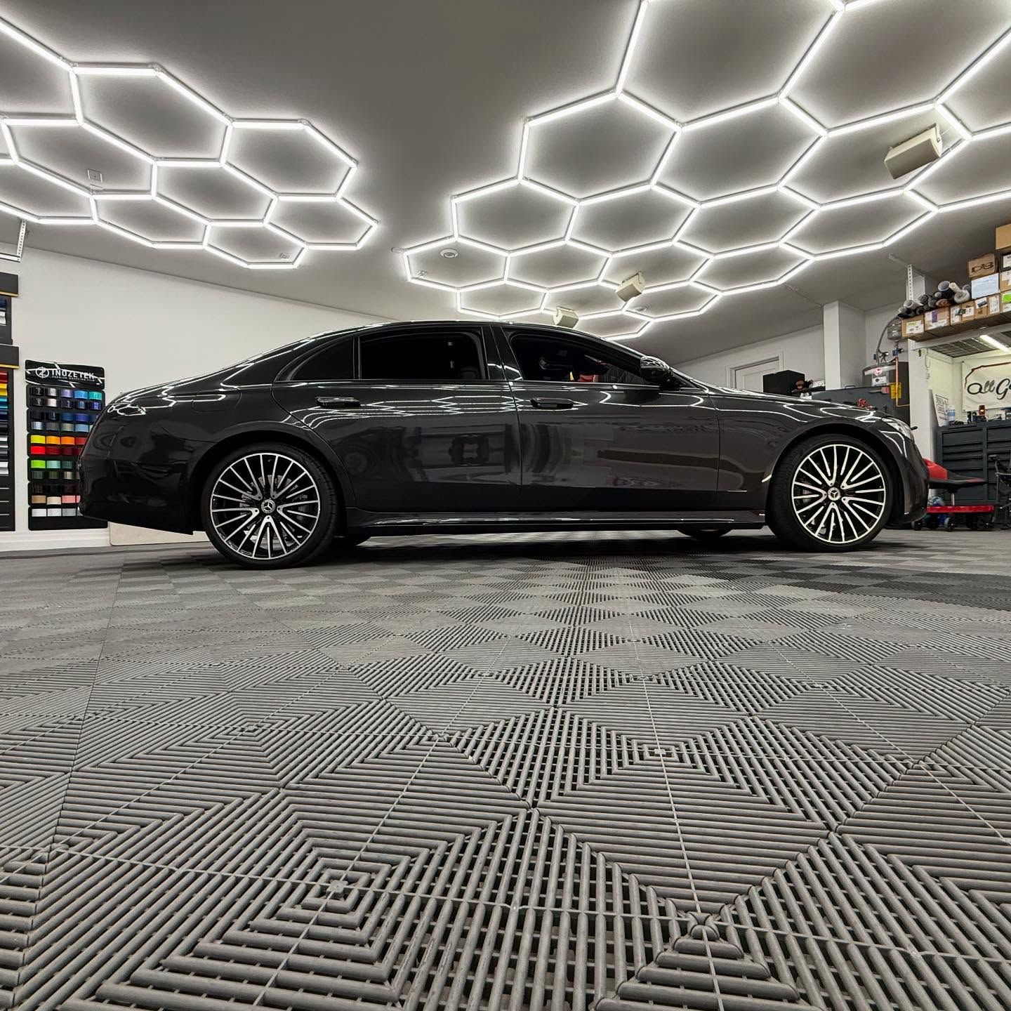 Dark gray sedan parked on a tiled floor in a brightly lit garage.