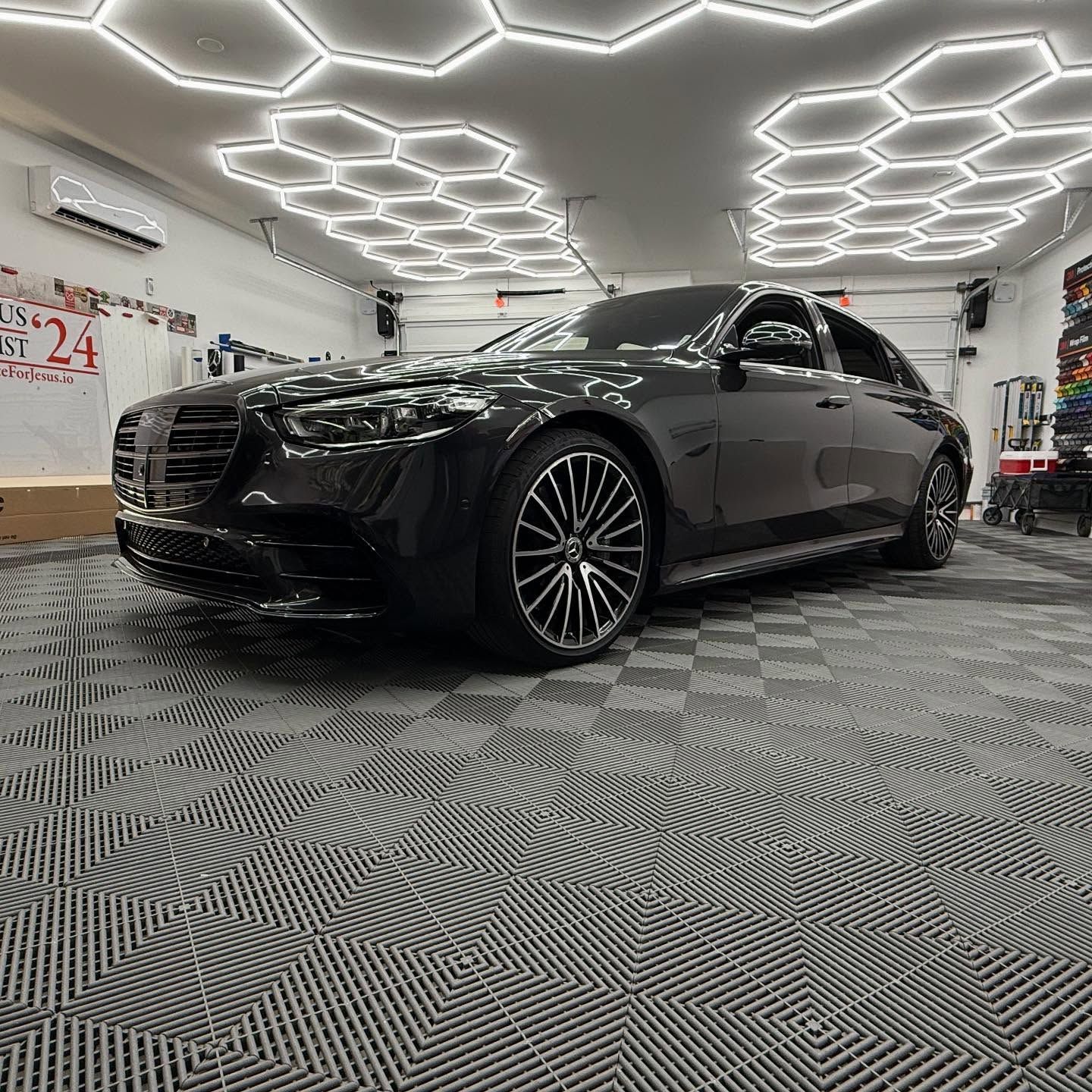 Dark Mercedes sedan parked in a well-lit garage with honeycomb ceiling lights and checkered floor.
