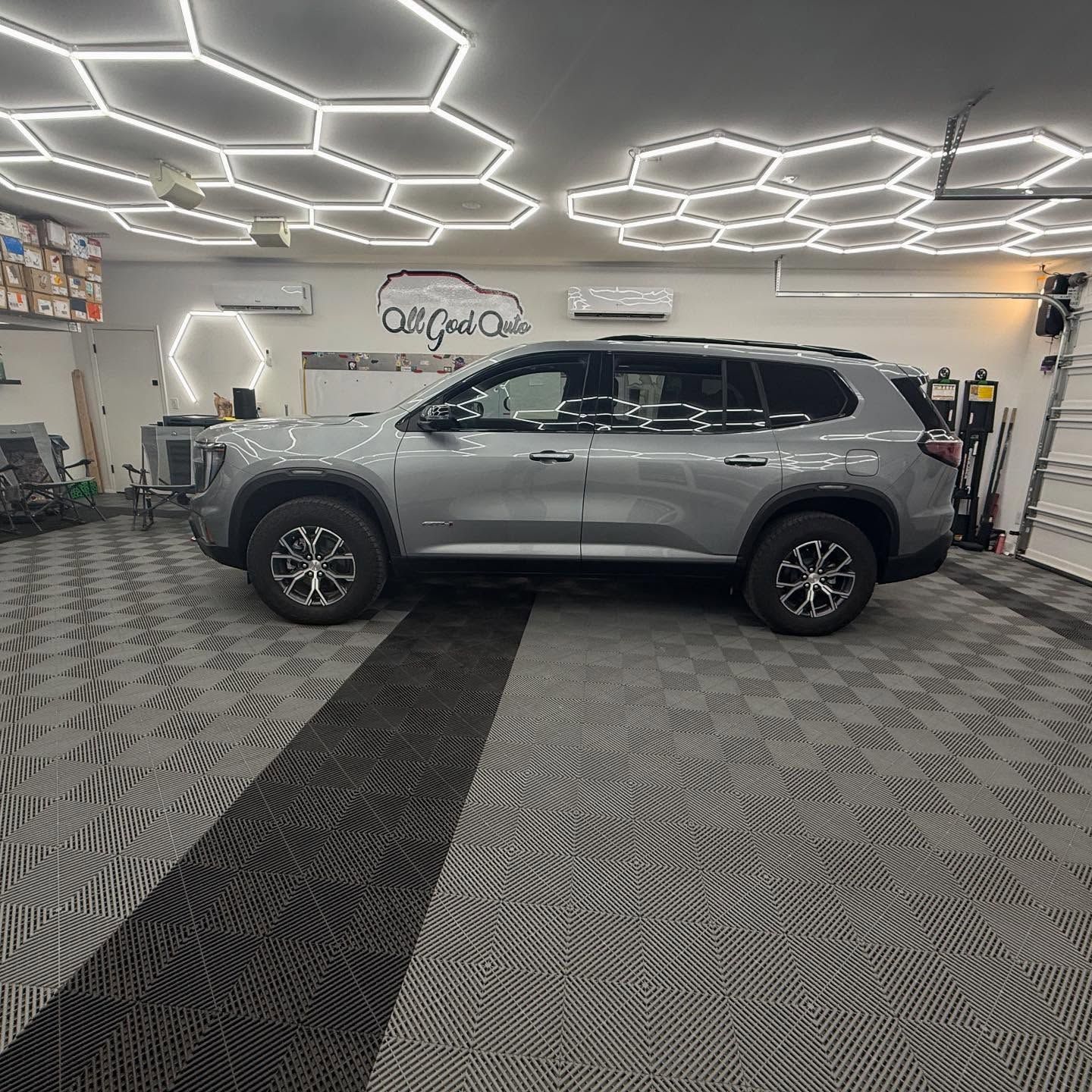 Gray SUV parked in a garage with hexagonal ceiling lights and patterned floor.