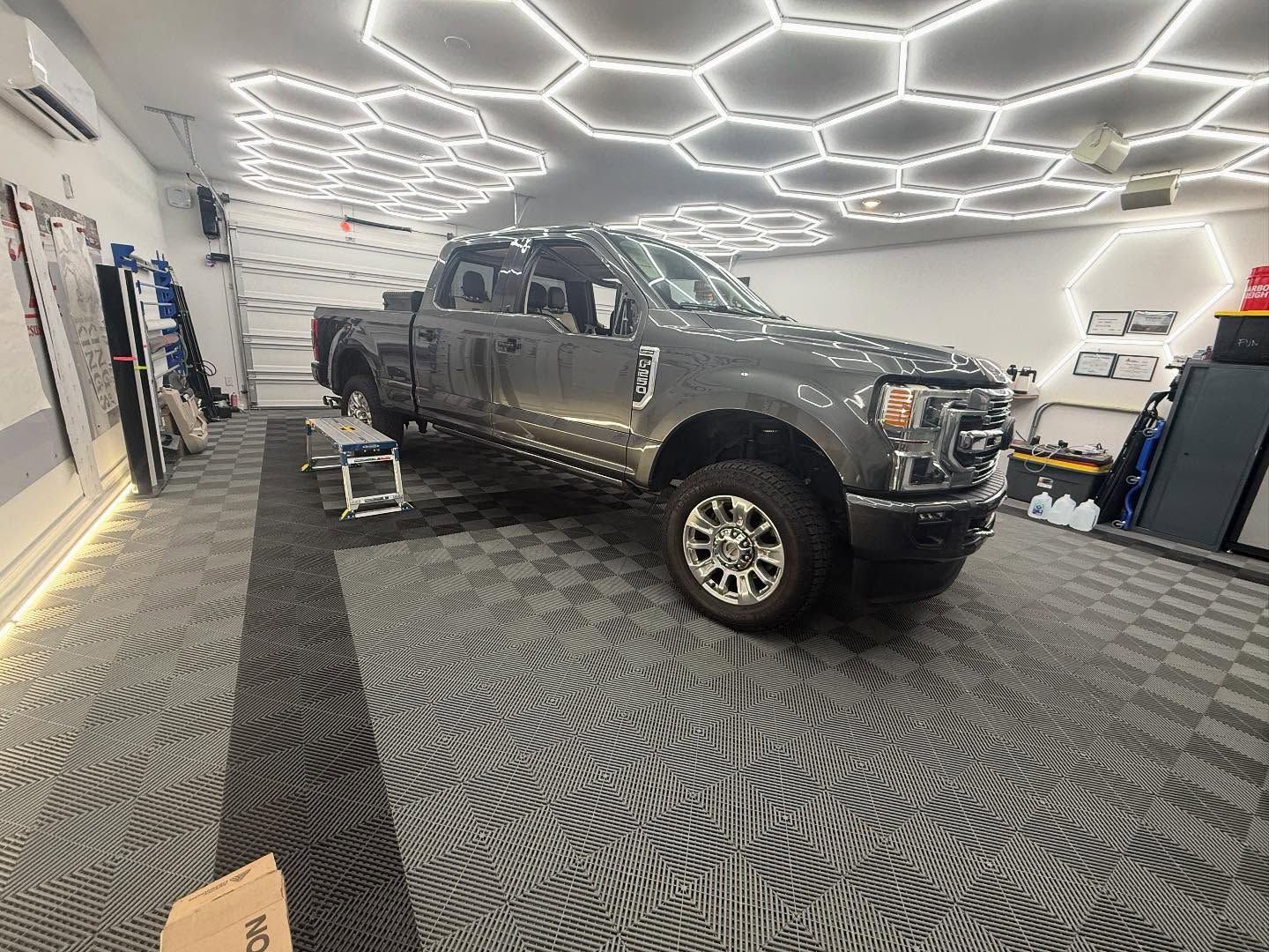 Gray pickup truck inside a well-lit garage with hexagon ceiling lights and gray patterned floor tiles.