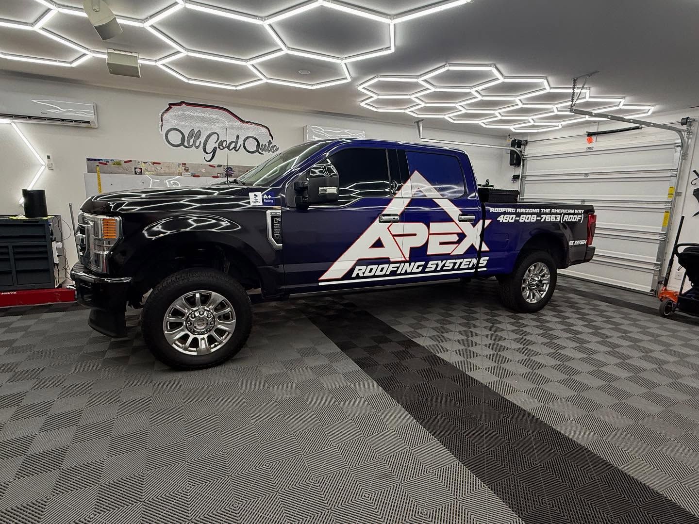 Black and blue Apex Roofing truck parked inside garage with hexagon lights.