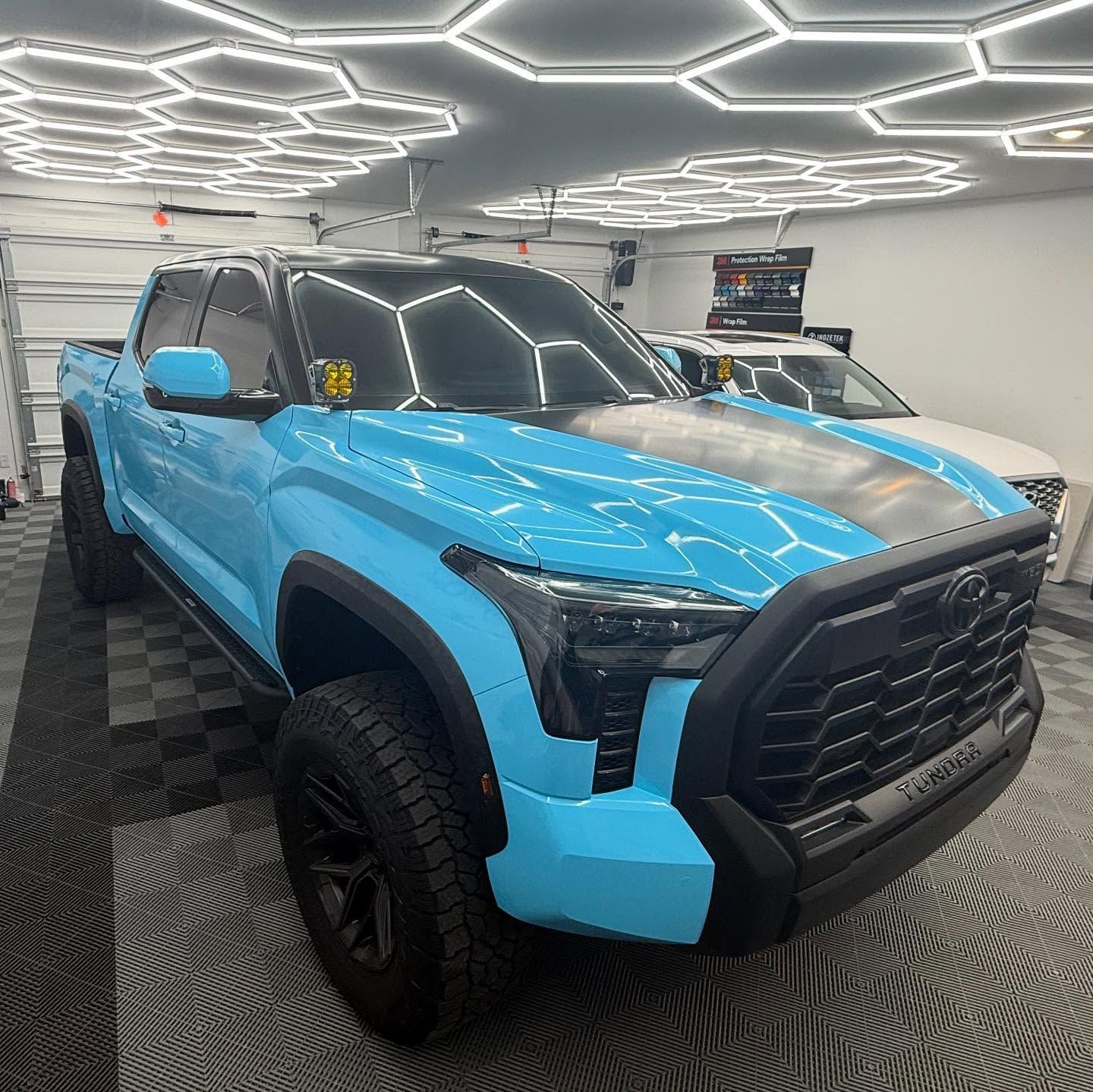 Bright blue lifted Toyota Tundra with black accents parked indoors under hexagon lights.