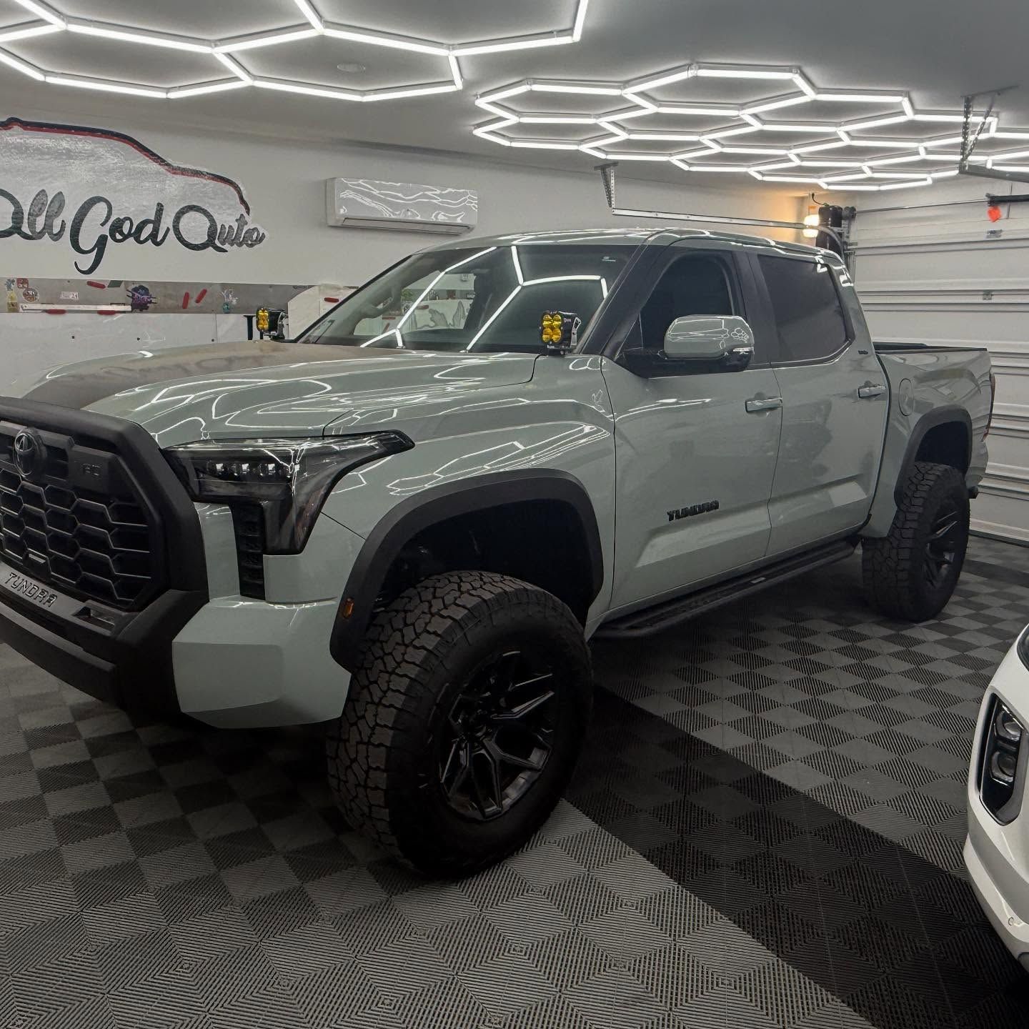 Gray Toyota Tundra truck with black wheels in a garage with honeycomb lighting.