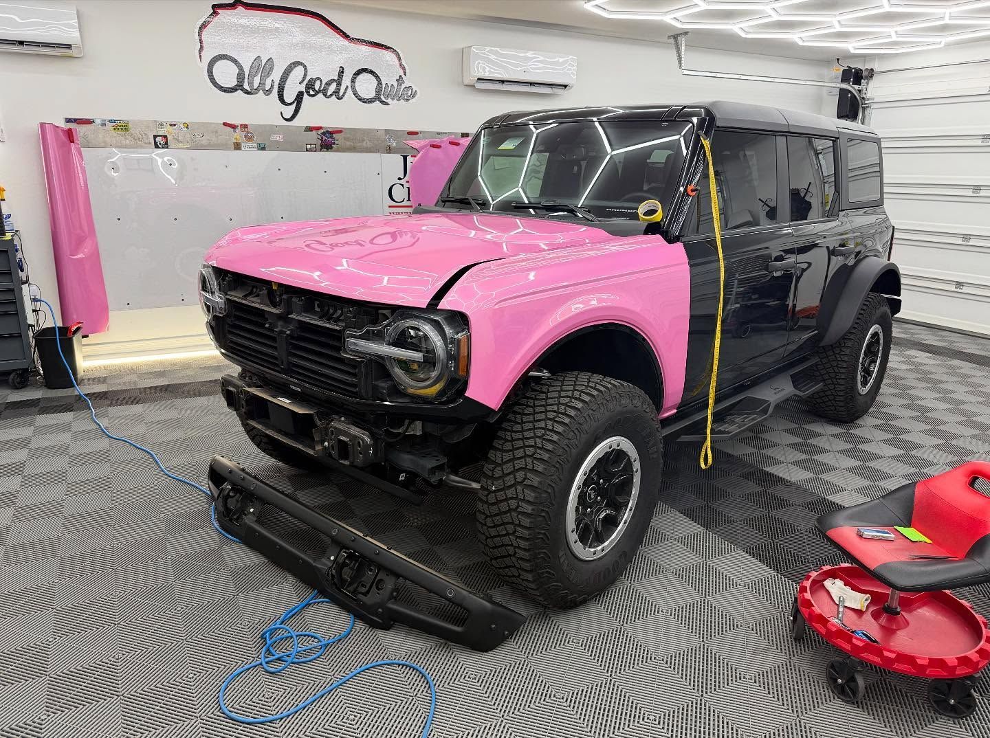 Black and pink Ford Bronco being worked on in a shop. Its hood and part of the side are pink.