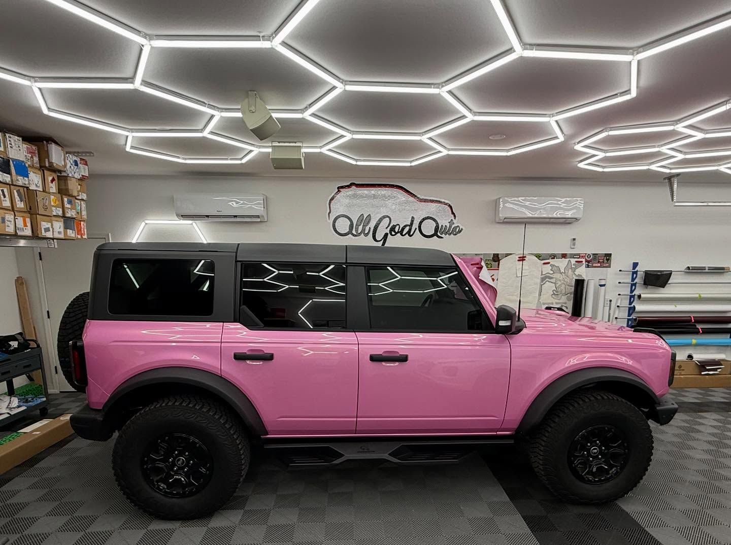 Pink Ford Bronco with black accents inside a shop.