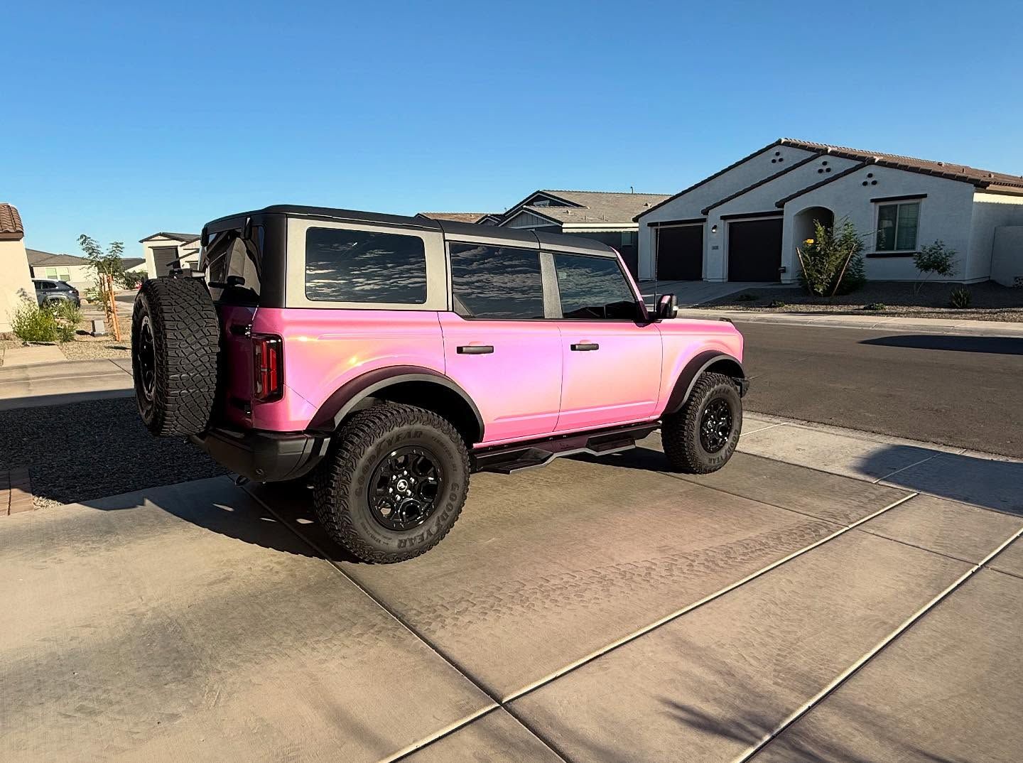 Pink Ford Bronco with black wheels parked on a driveway in front of a residential home.