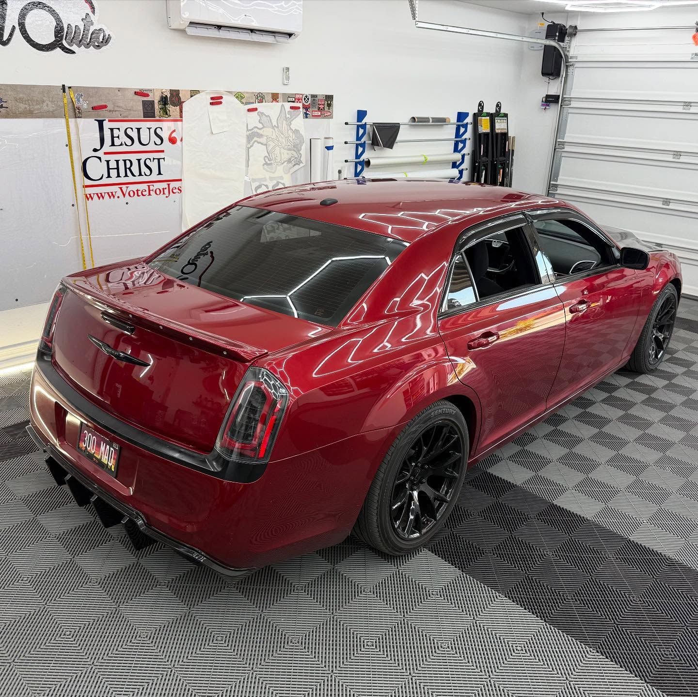 Red Chrysler 300 sedan with black wheels inside a garage.