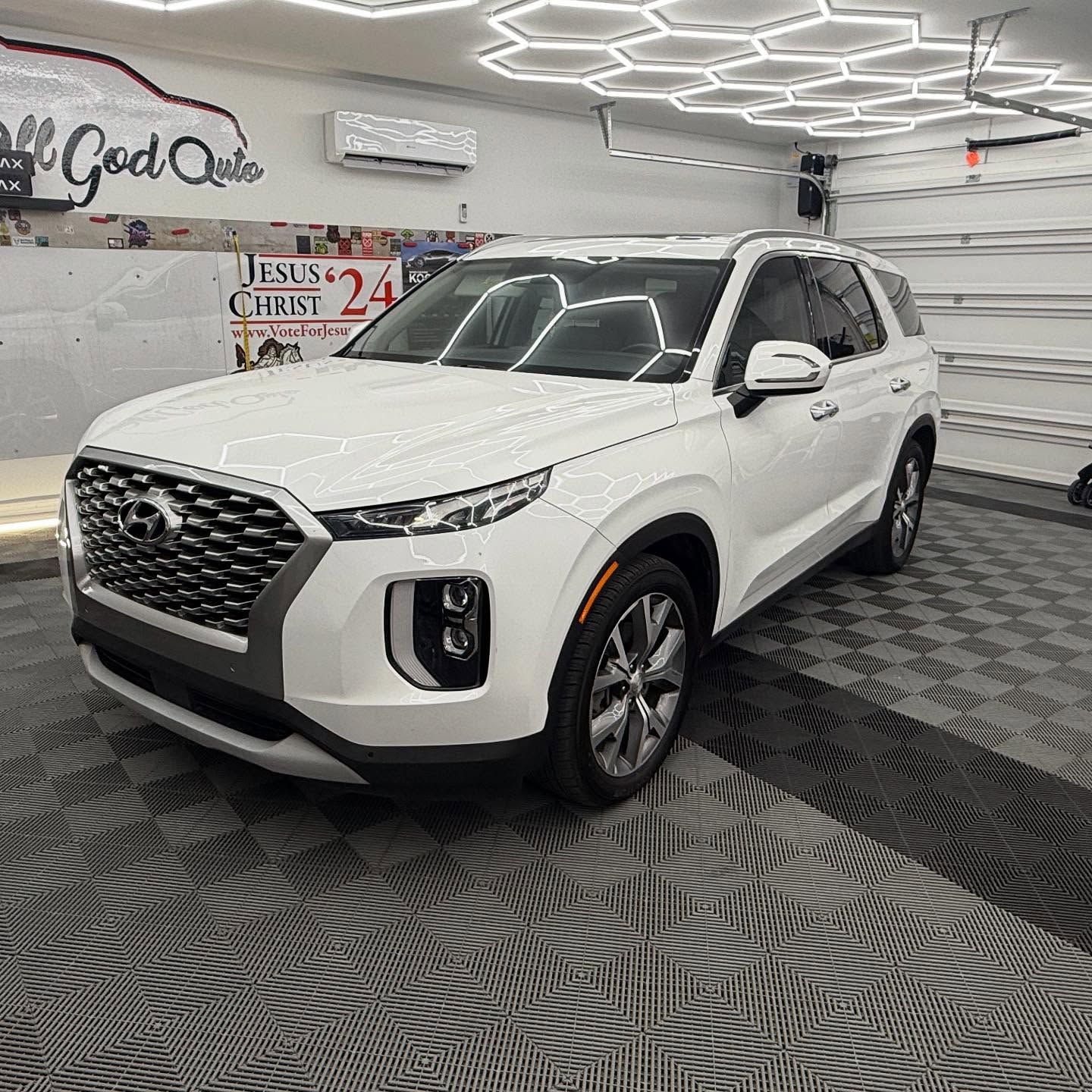 White Hyundai Palisade SUV parked on a checkered floor, lit by overhead hexagonal lights.