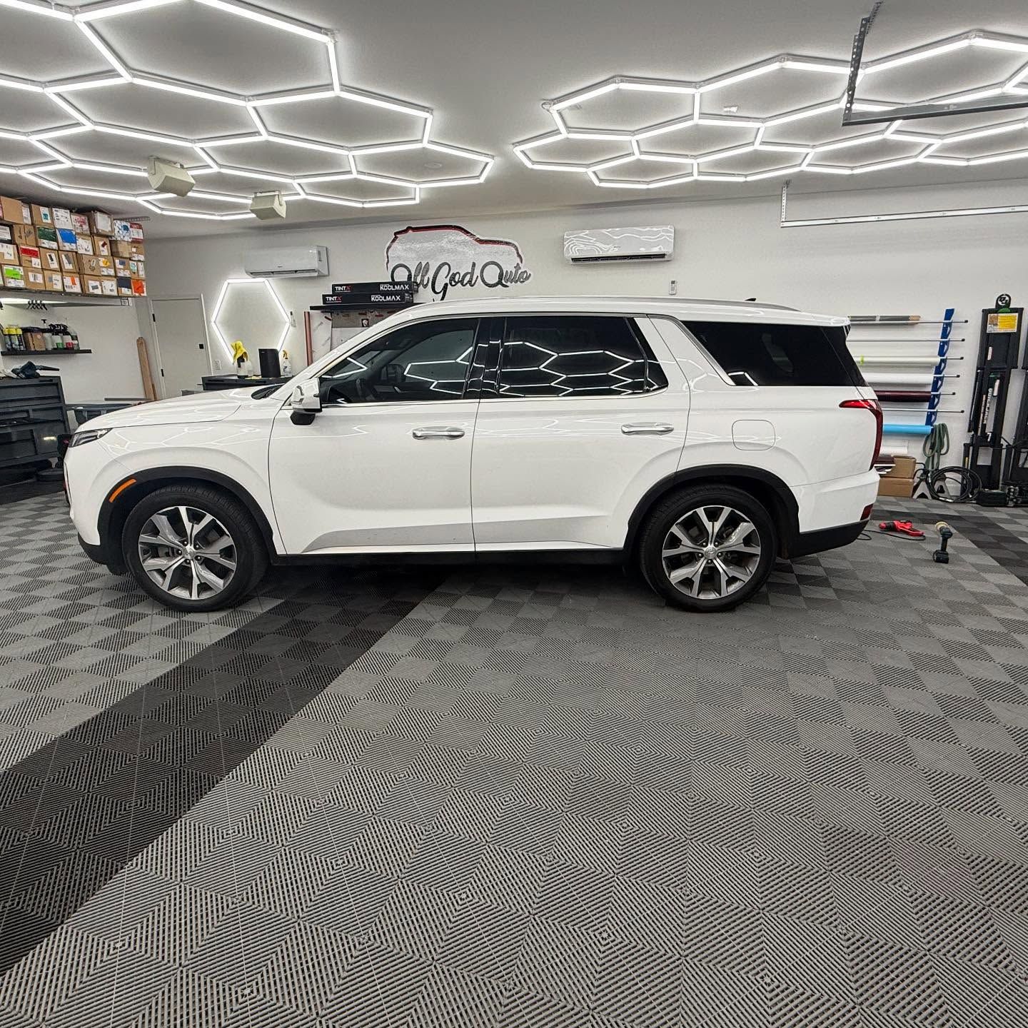 White SUV in a well-lit shop with hexagon-shaped lights, black and gray flooring, and tinted windows.