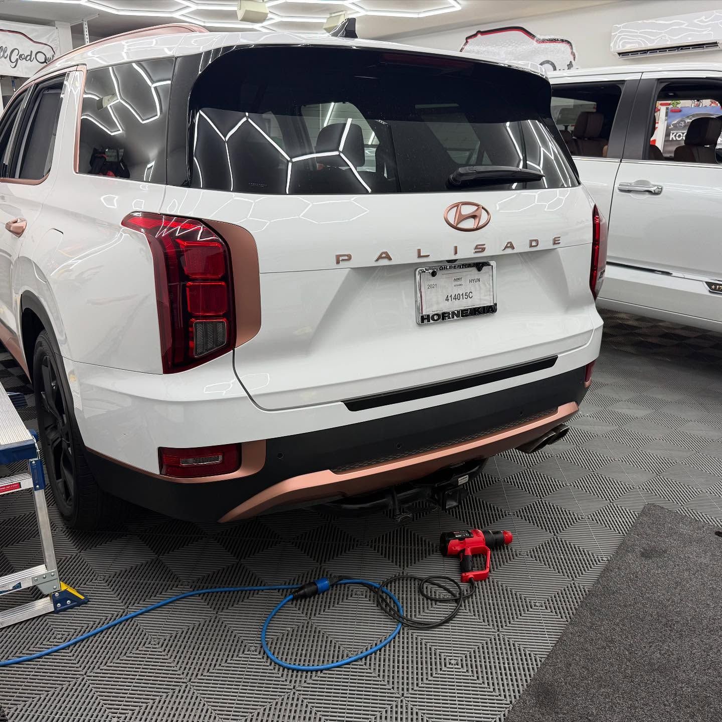 White Hyundai Palisade with copper accents in a garage, angled view of the rear.