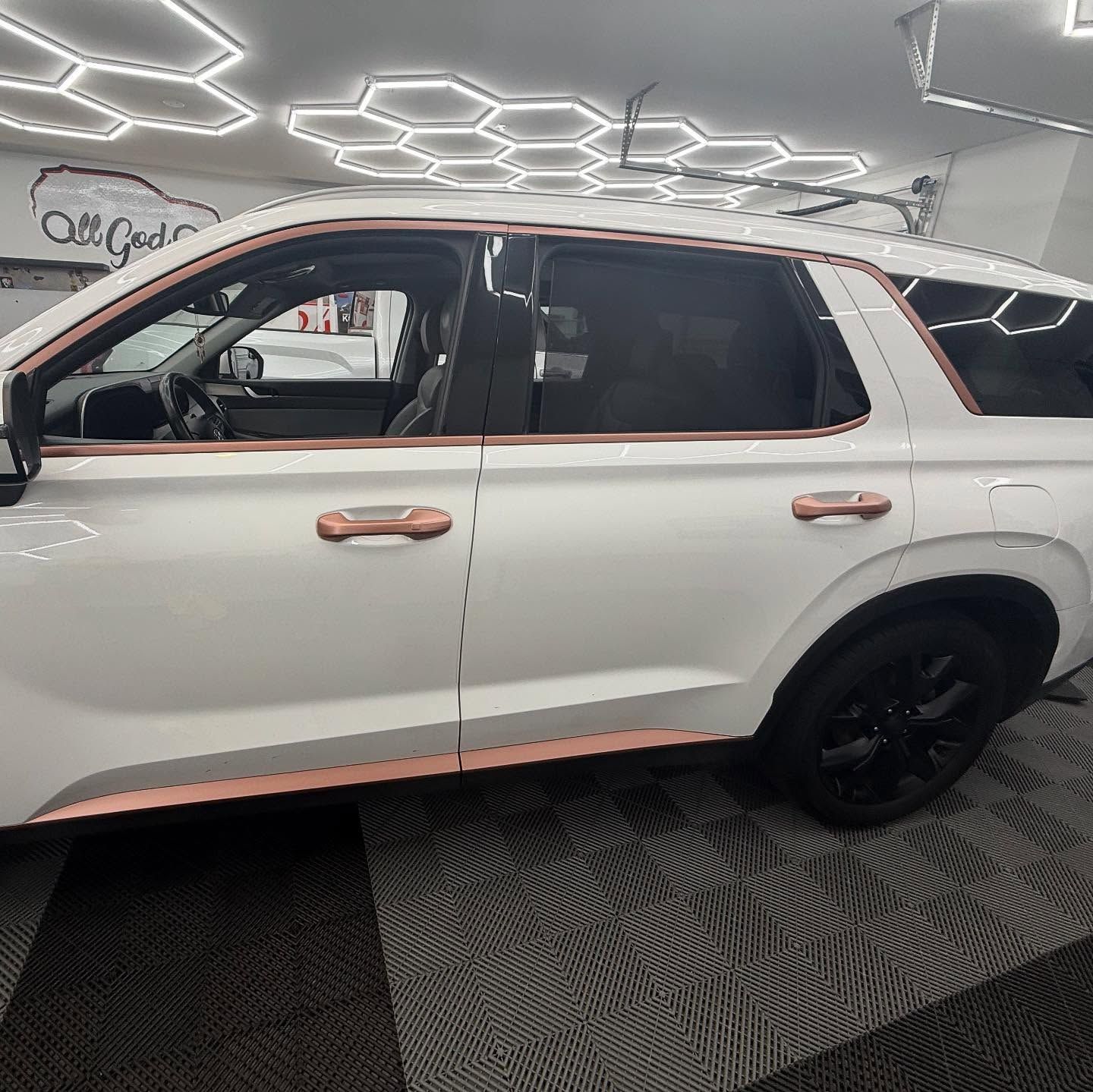 White SUV with rose gold trim and black wheels in a brightly lit garage.