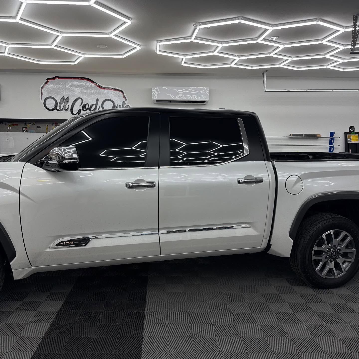 White Toyota pickup truck with tinted windows parked indoors under hexagonal lights.
