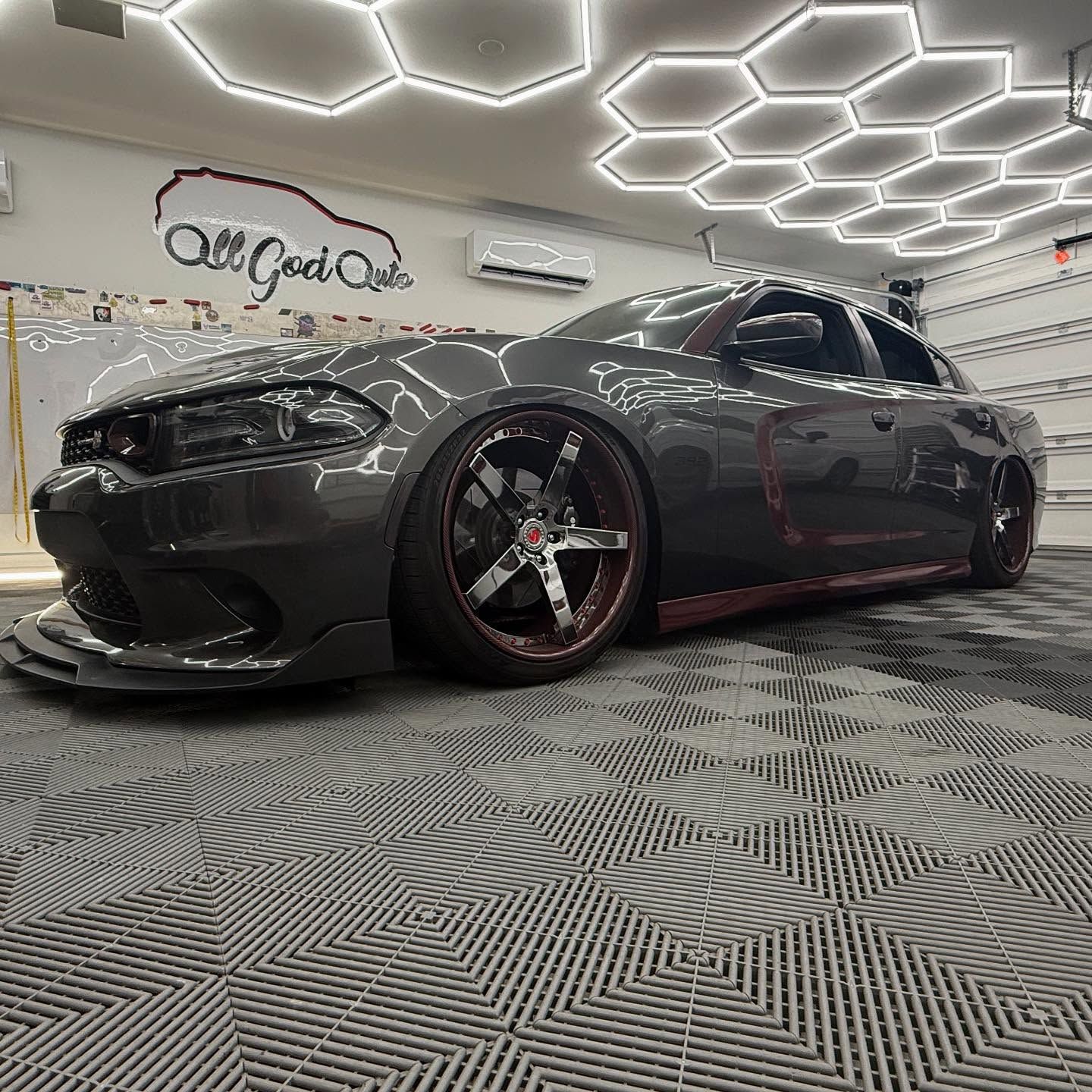 Gray Dodge Charger on custom wheels, in a car detailing shop with hexagon lights and tile floor.