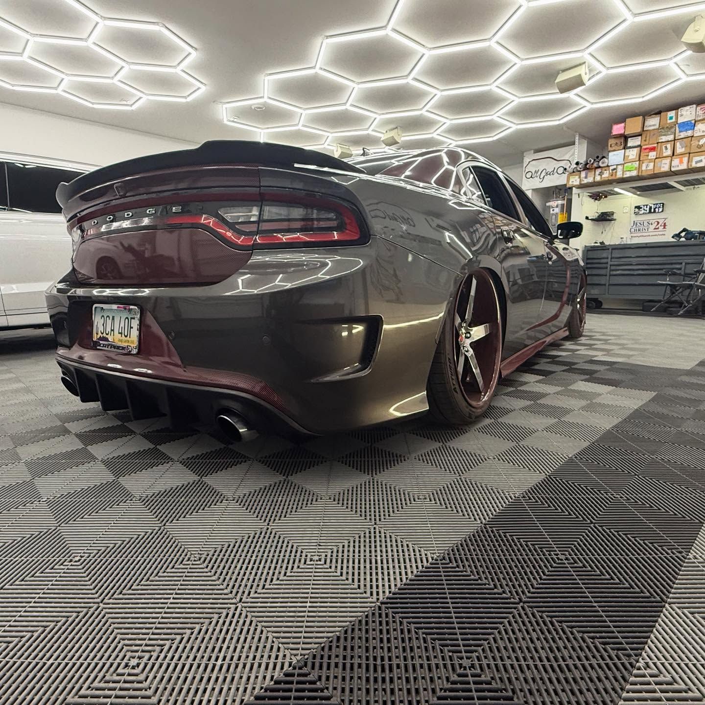 Gray and maroon Dodge Charger on tiled floor, low rider with red accents, under hexagon lights.