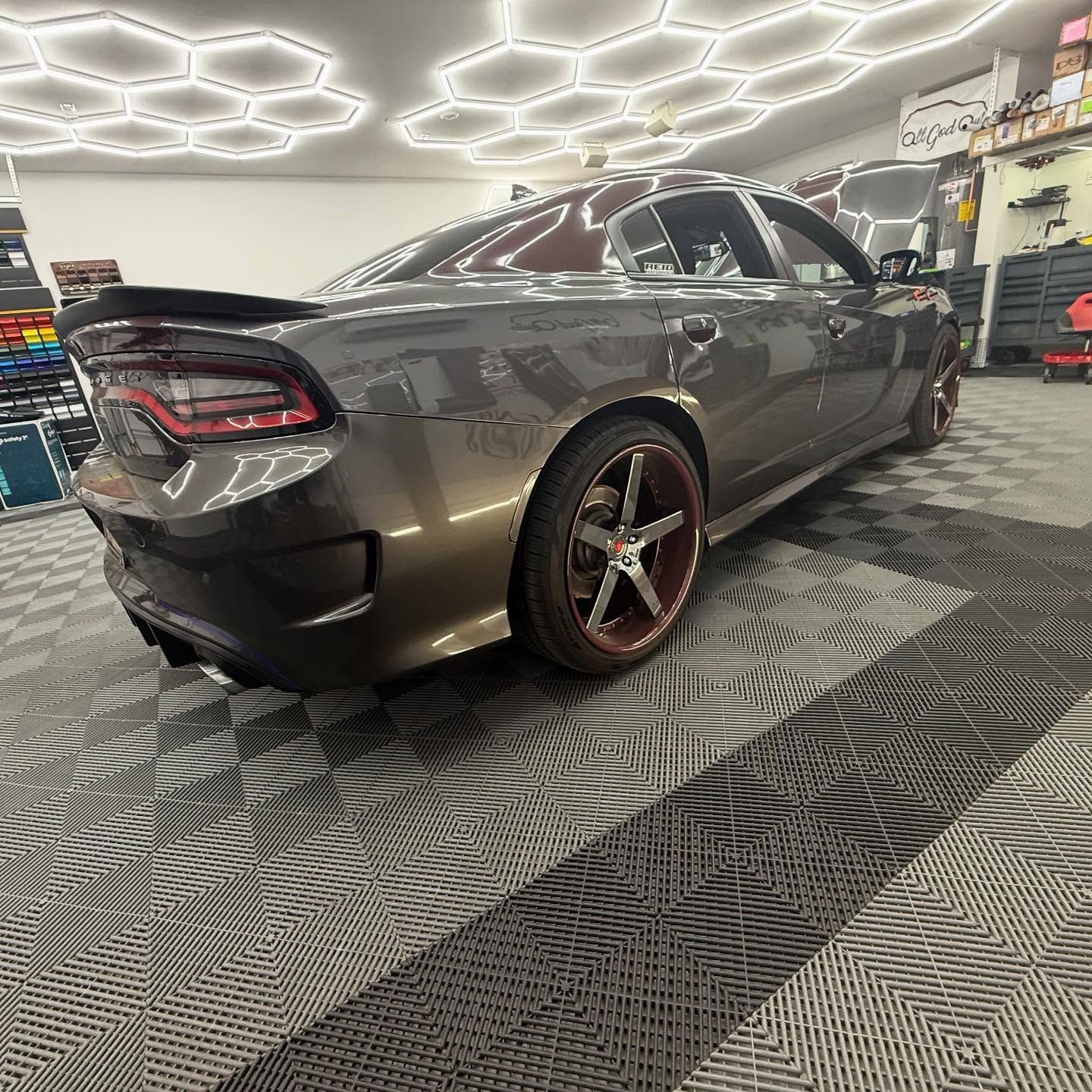 Gray Dodge Charger with custom wheels inside a garage, under bright lights.