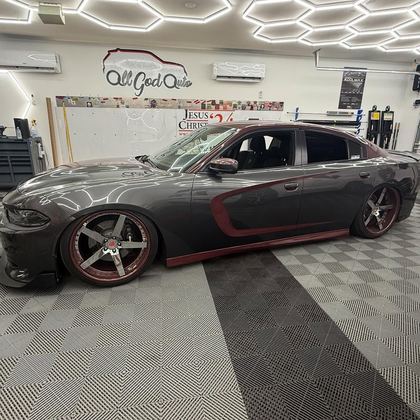 A custom gray Dodge Charger with maroon accents parked inside a car shop.