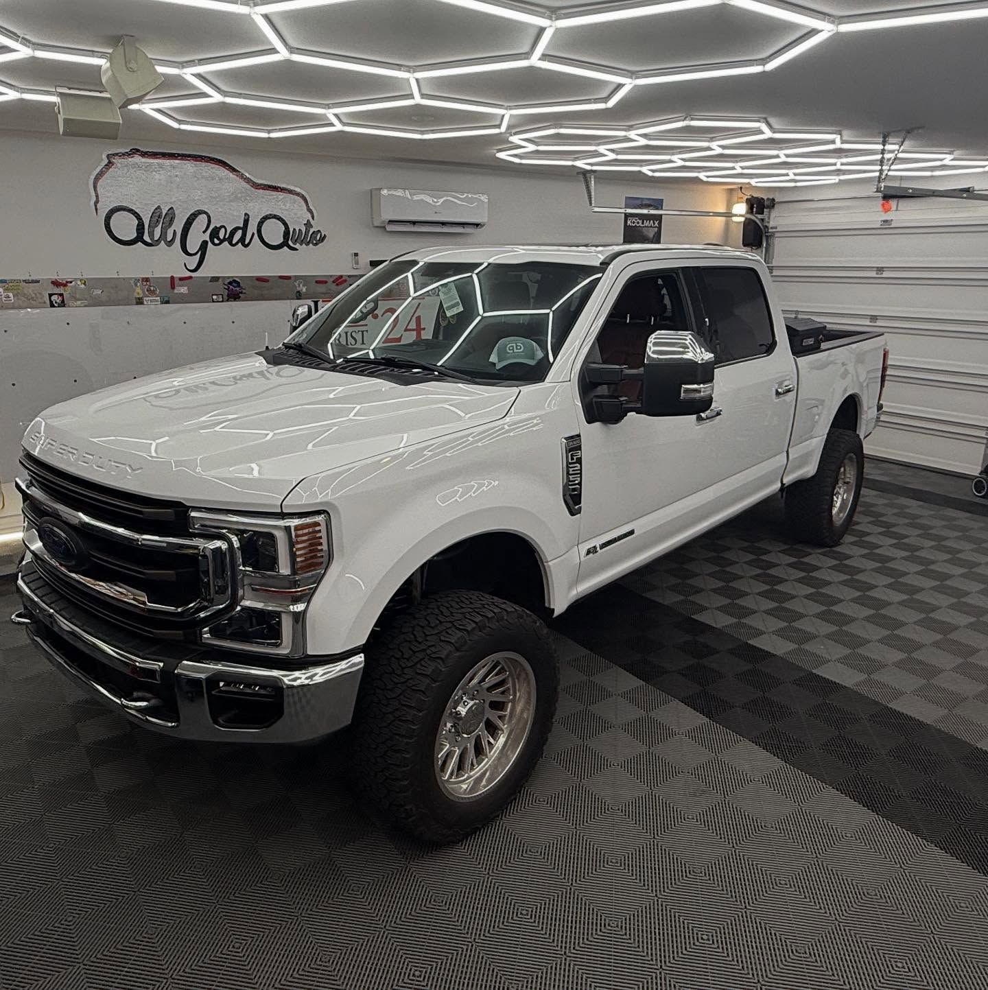 White Ford pickup truck in a well-lit garage with black and gray flooring.