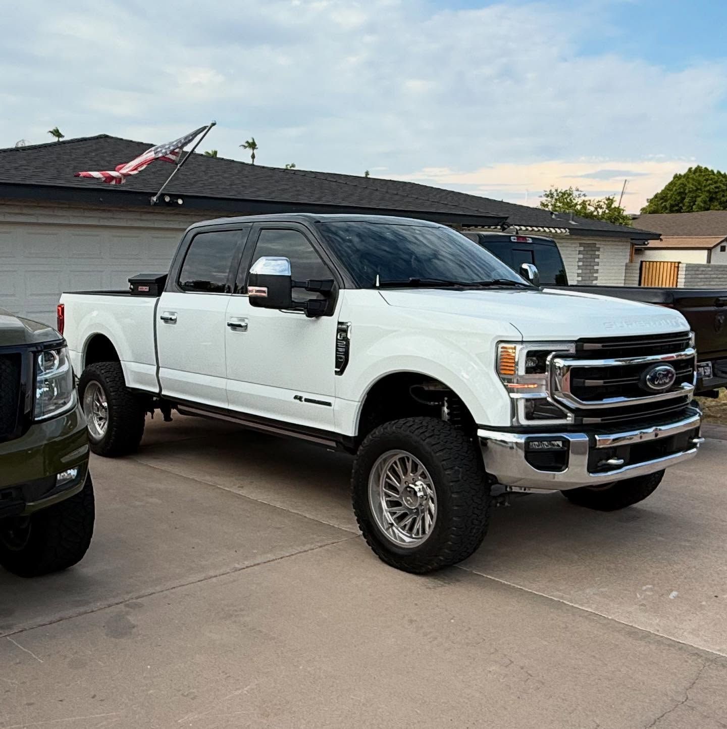 White Ford F-350 truck with black roof, lifted suspension, parked on concrete.