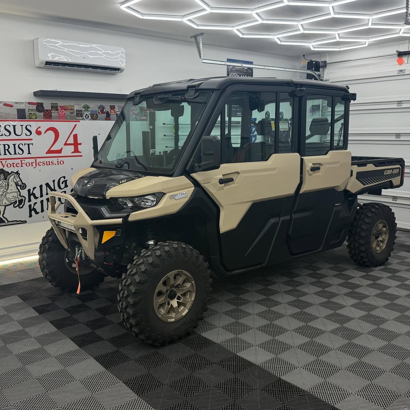 Tan and black side-by-side utility vehicle in a garage, with large off-road tires, and enclosed cab.