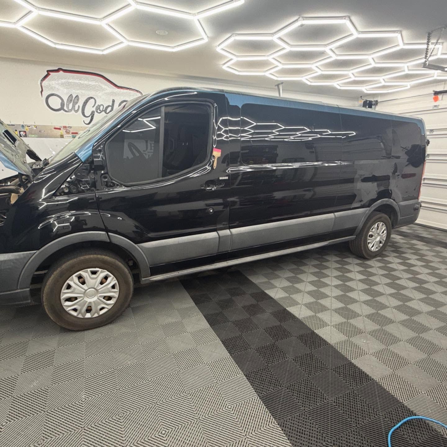 Black van with tinted windows parked inside a garage with checkered floor and hexagonal lights.