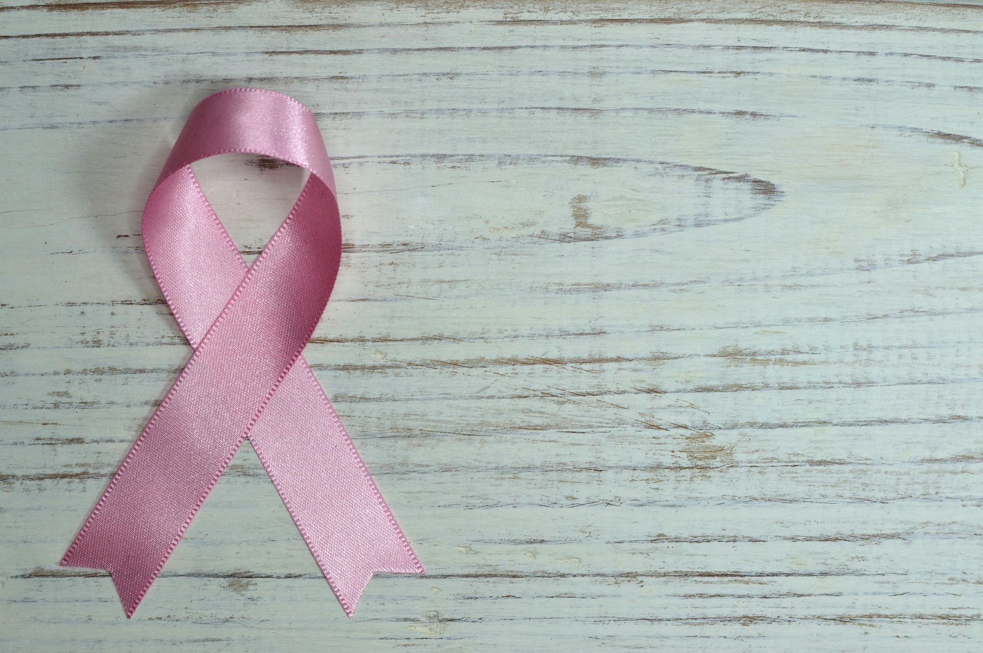 Pink awareness ribbon on a weathered white wooden surface.