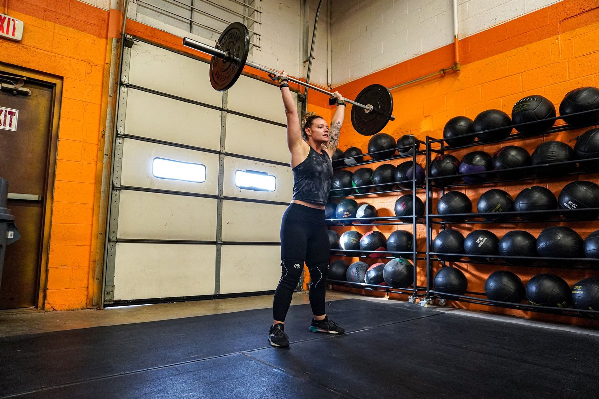 A woman is lifting a barbell over her head in a gym.