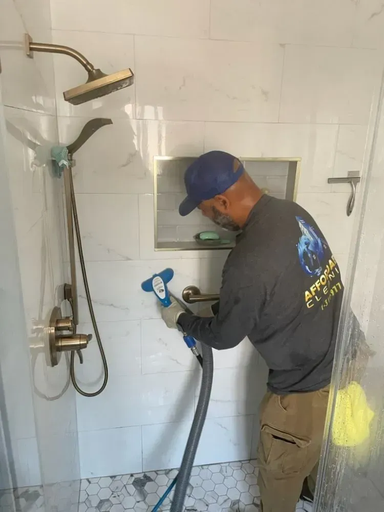 A man is cleaning a shower with a vacuum cleaner.