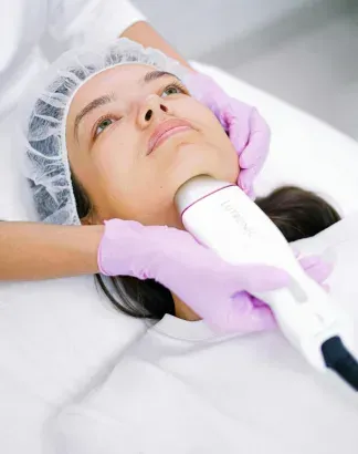 Woman receiving a facial treatment while lying on a spa bed, with purple-gloved hands holding a handheld device