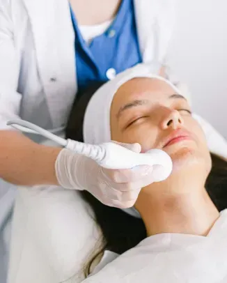 A clinician applies a facial treatment device to a reclining patient in a spa setting.