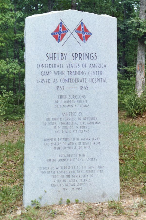 A gravestone for shelby springs is surrounded by grass and trees