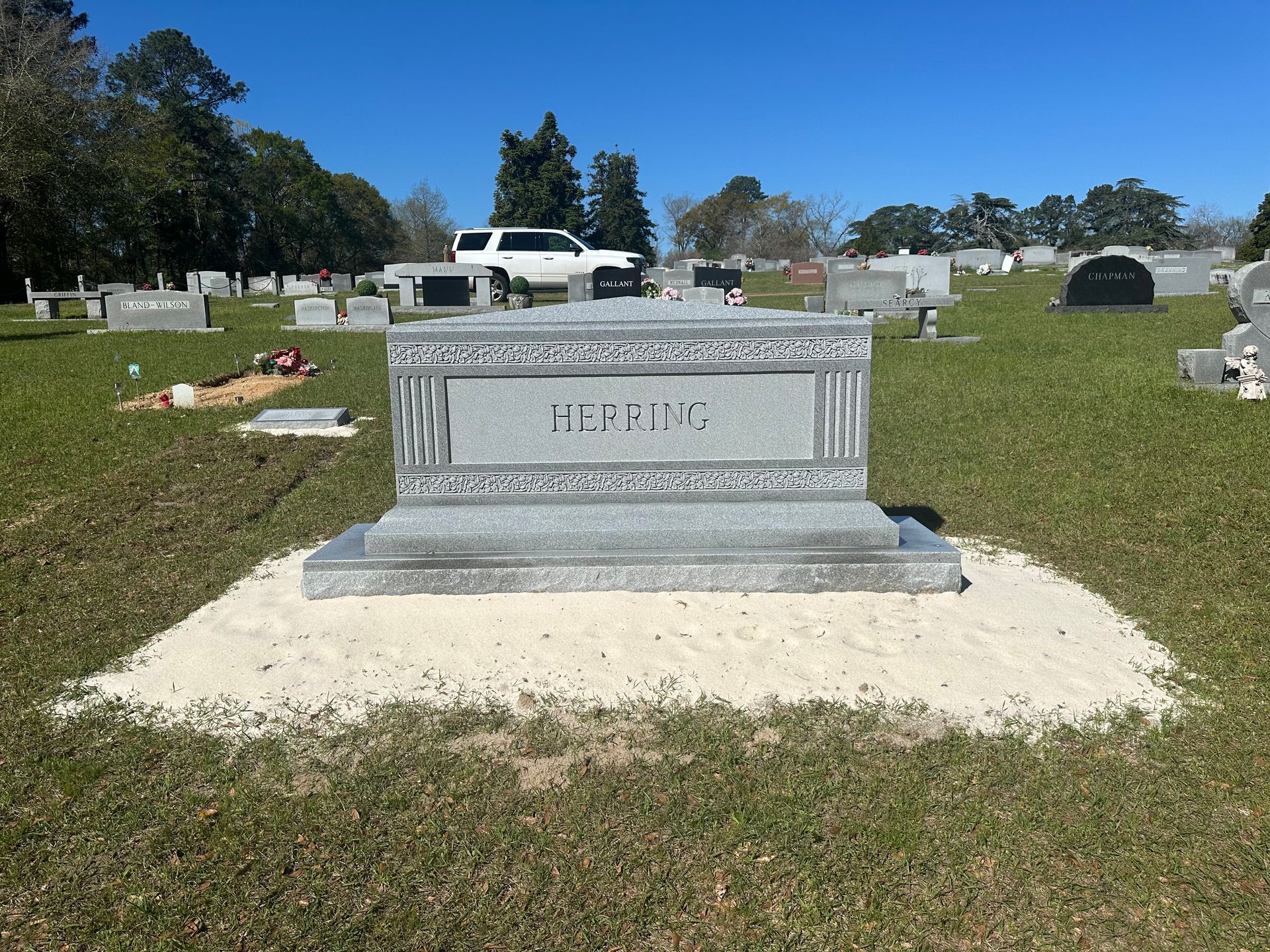 A grave in a cemetery with a car parked in the background