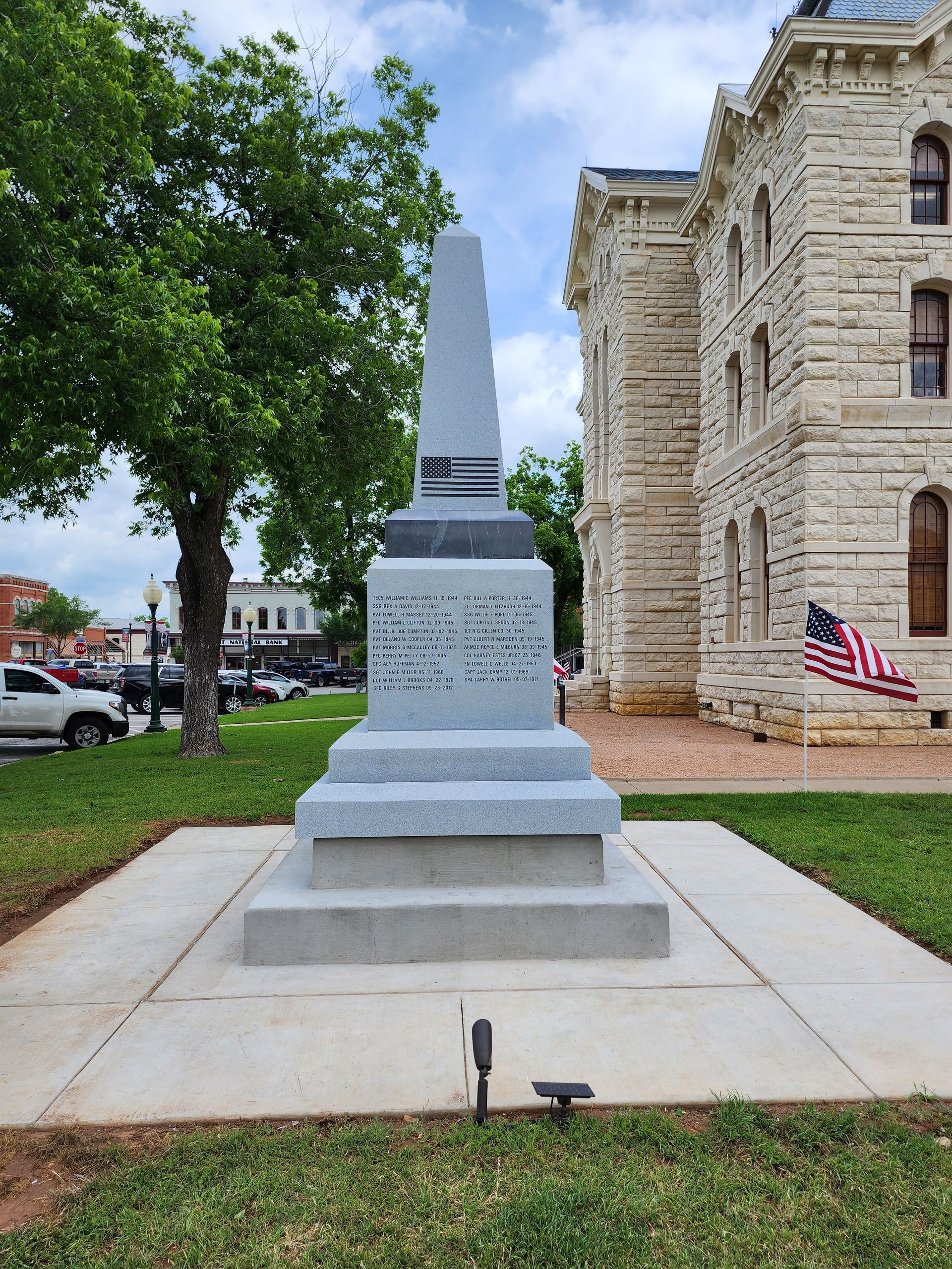 A memorial in front of a brick building with an american flag flying in the background.