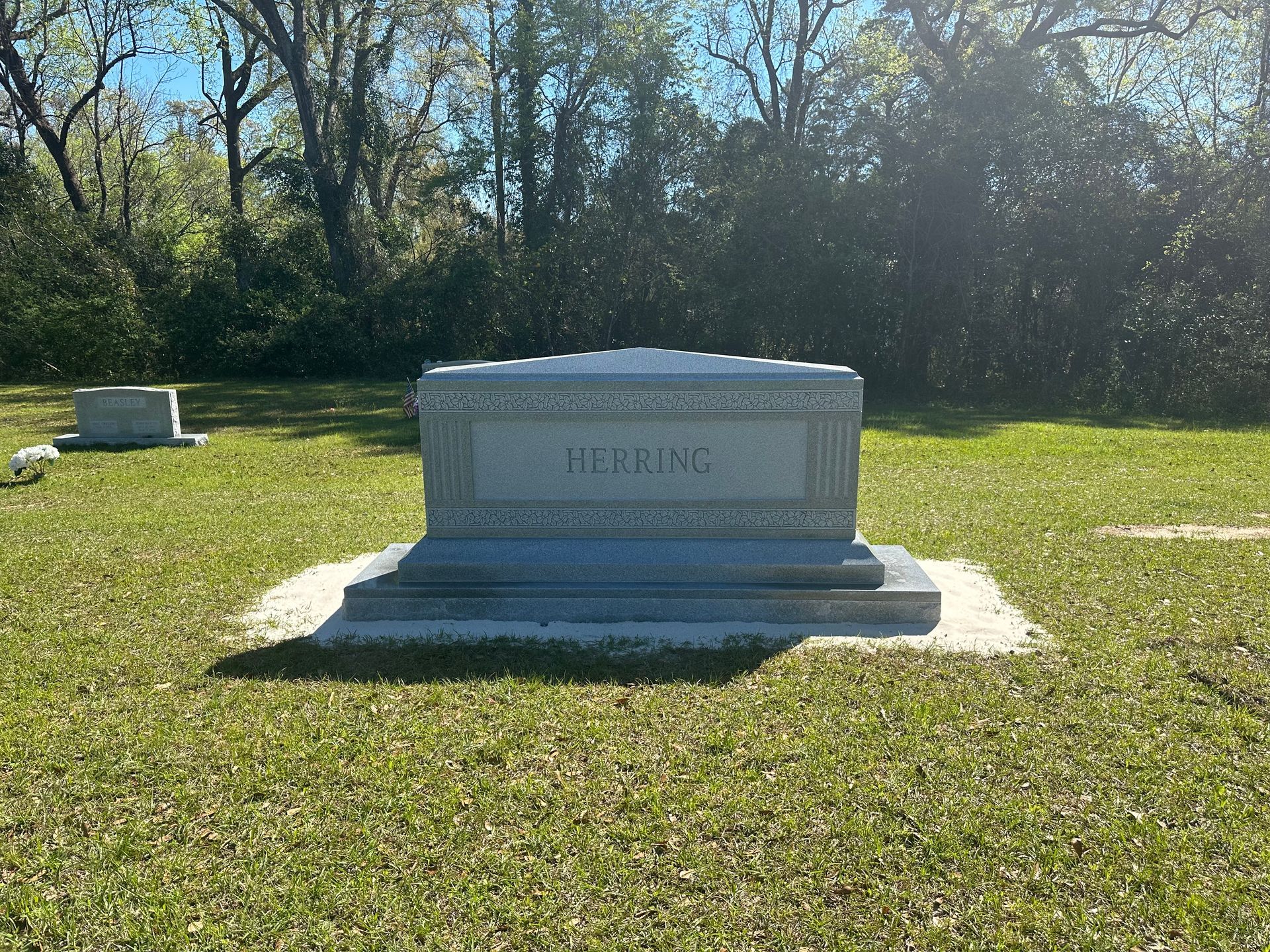 A grave in a grassy field with trees in the background.