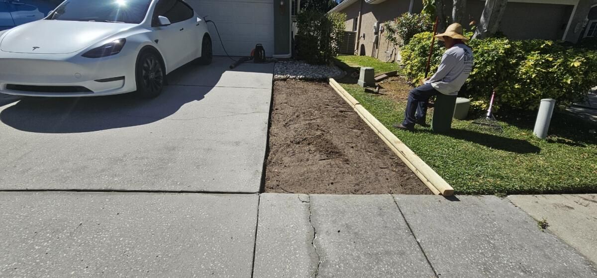 A white tesla model y is parked in a driveway next to a man in a hat.