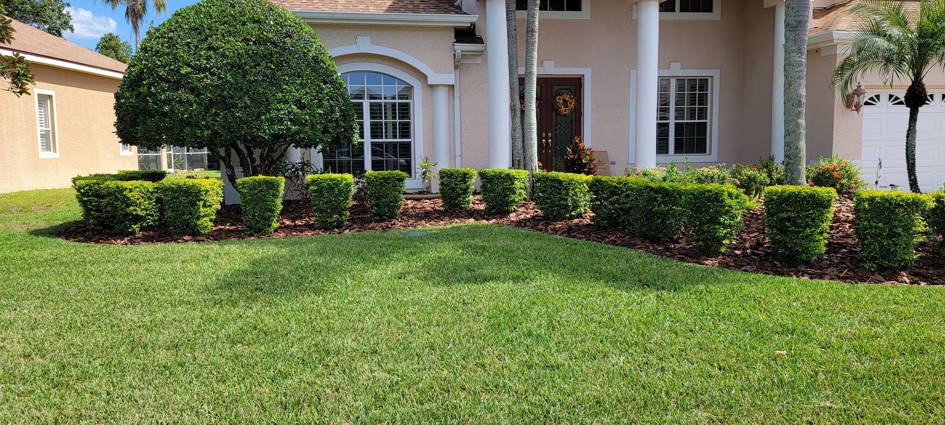 A house with a lush green lawn and bushes in front of it.