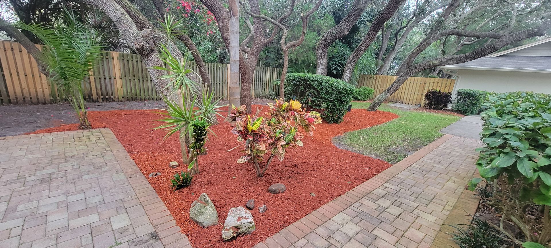 A brick walkway leading to a backyard filled with lots of plants and trees.