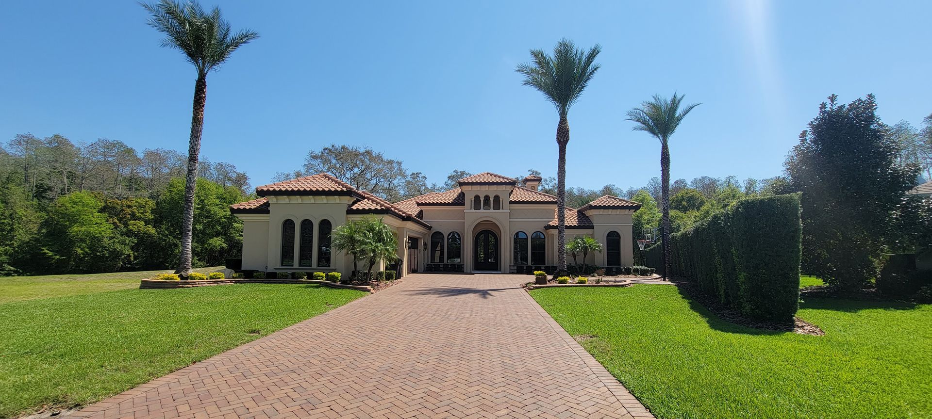 A large house with a brick driveway and palm trees in front of it.