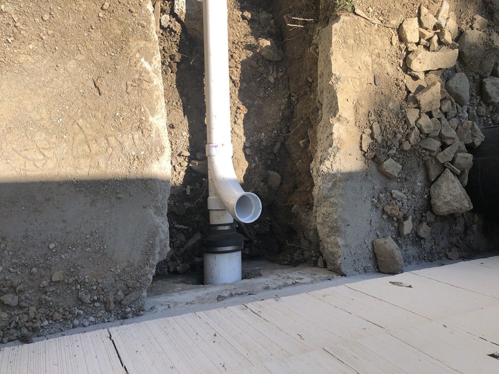 A white pipe is sitting in the dirt next to a wall.
