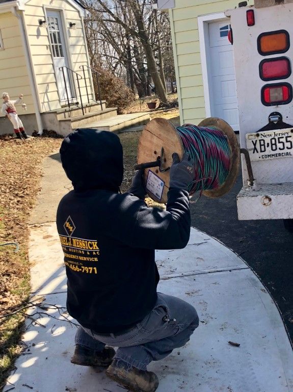 A man is kneeling down next to a truck holding a spool of wires.