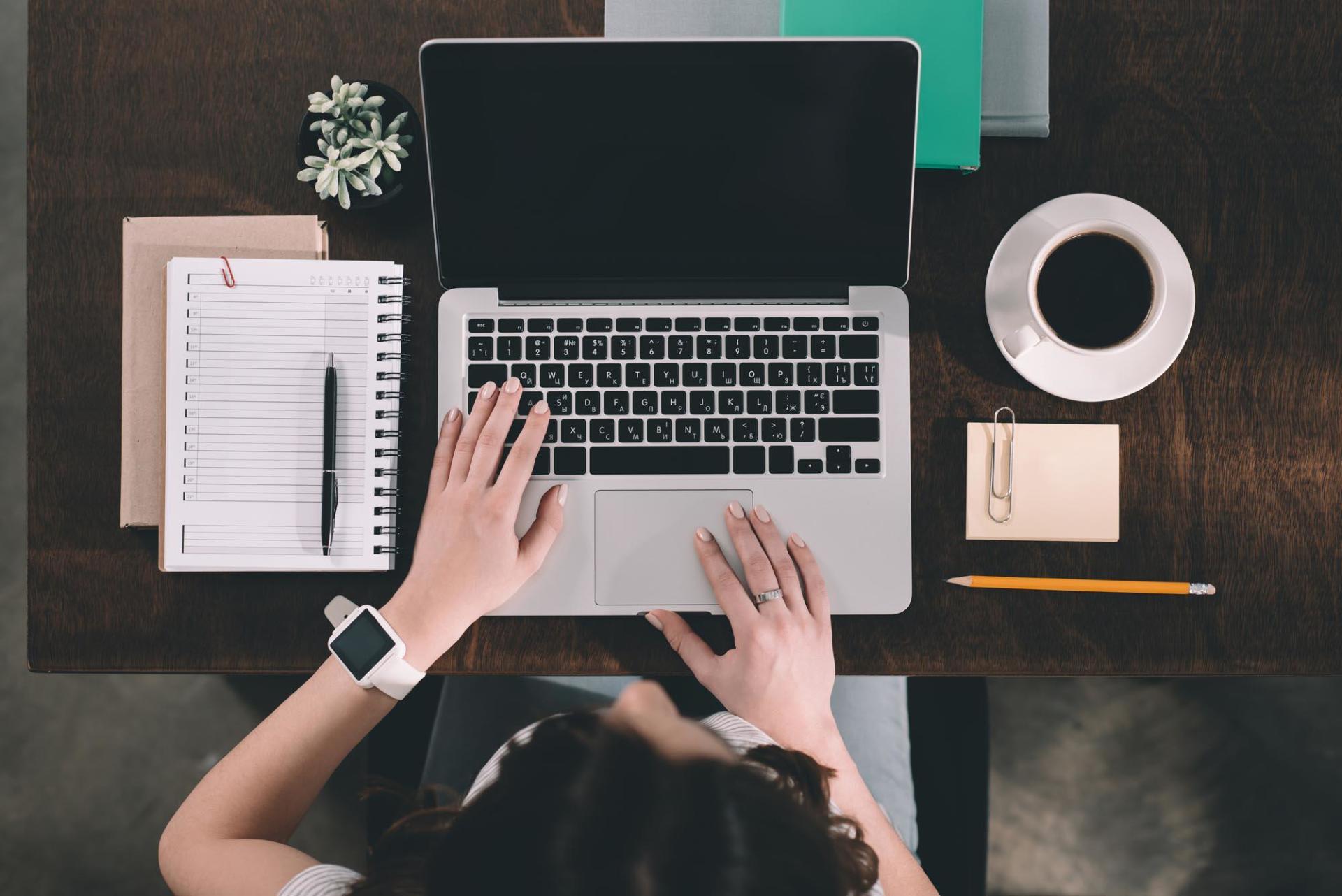 A woman is typing on a laptop computer at a desk.
