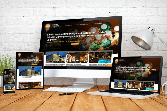 Website displayed on various devices: phone, tablet, desktop, and laptop, on a wooden desk.